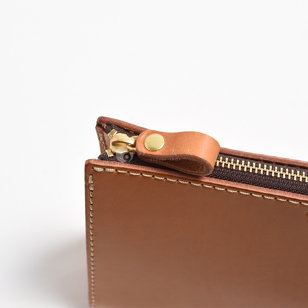 職人手作皮革三角底拉鍊手拿包，採用棕色皮革，搭配金色拉鍊與銅扣。包包邊緣有手工縫線，質感細膩。