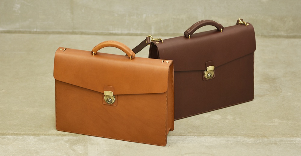兩個職人手作皮革Organ兩用商務公事包，一個為淺棕色，一個為深棕色，皆採用經典公事包設計，配有頂部提把、金屬鎖扣及可拆卸肩帶。