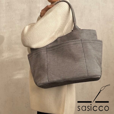 一位女士身穿米白色針織衫，肩背一個黑色與白色格紋圖案的刺子織手提托特包。