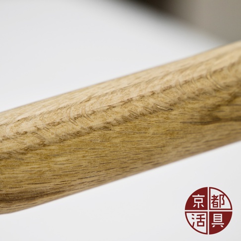 近距離特寫，展示一個淺棕色木質鍋柄，表面有明顯的木紋和細膩紋理。右下角有一個紅底白字的圓形標誌，標誌內有「京都」和「活具」字樣。