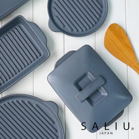 深灰色帶蓋陶製烤盤，表面有烤紋，配有木製鍋鏟，陳列於白色木紋背景上。