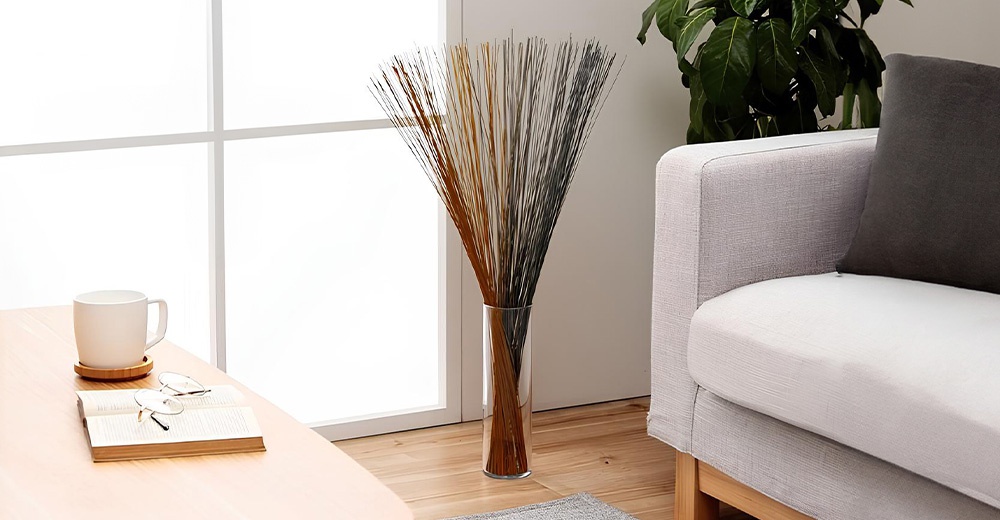 書桌上放著一杯咖啡和一本書，後方是一個大型花瓶，裡面插著大量深棕色和黑色的細長裝飾物，旁邊是舒適的灰色沙發，沙發上有一個深灰色抱枕。