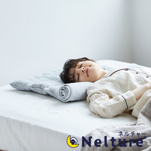 淺灰色毛巾布材質的枕頭，一端捲起，一位女性仰臥在床上，頭部枕於其上。