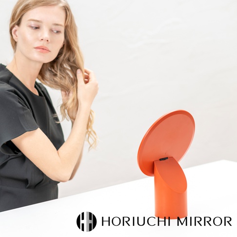 橘色圓形桌面化妝鏡，鏡面可調節，底座為圓柱形，材質為塑膠。