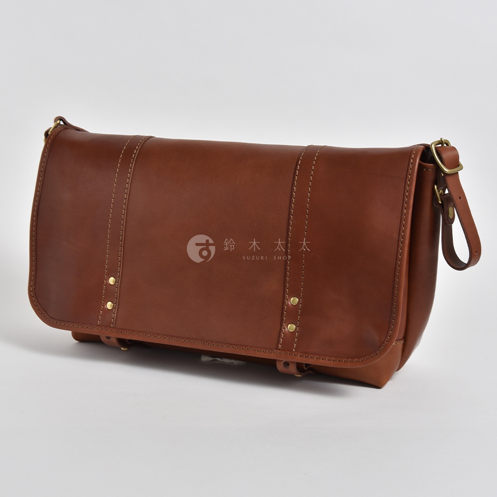 職人手作復古皮革郵差包，採用棕色皮革，帶有雙縫線細節和金色鉚釘，搭配金屬扣環和皮革背帶。