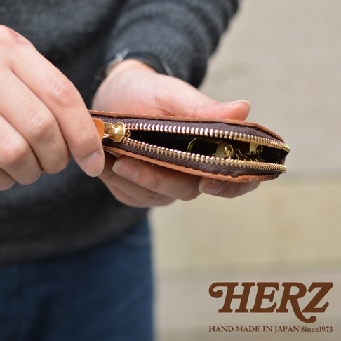 雙手正拿著一個打開的咖啡色皮革鑰匙包，露出內部的六個鉤子，包包上有著精緻的拉鍊和金屬配件。