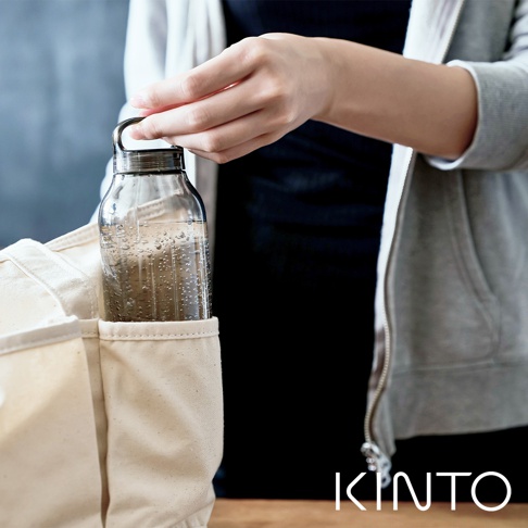 透明玻璃輕水瓶500ml，瓶身有細緻的條紋紋理，裝有氣泡水，瓶蓋為銀色金屬材質，帶有提環，瓶子被放置在米白色帆布袋的側邊口袋中。