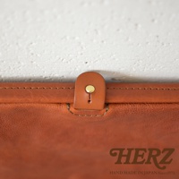 職人手作皮革Organ手拿包G-38，特寫皮革材質的翻蓋扣，附有金屬按鈕，皮革顏色為棕褐色，縫線精緻。