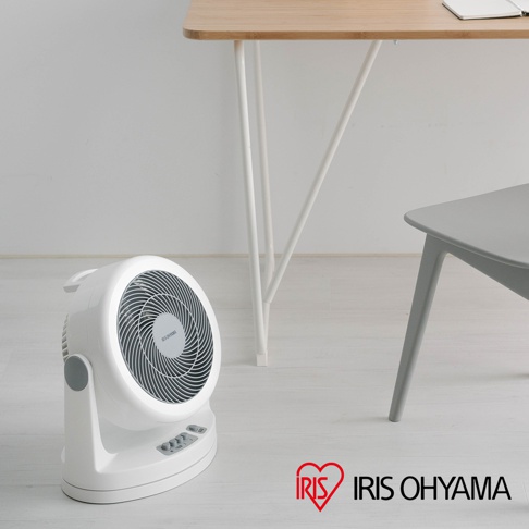 白色IRIS OHYAMA PCF-HM23 空氣循環扇，帶有銀灰色扇網和控制面板，放置在木質桌面和白色牆壁的房間地板上。