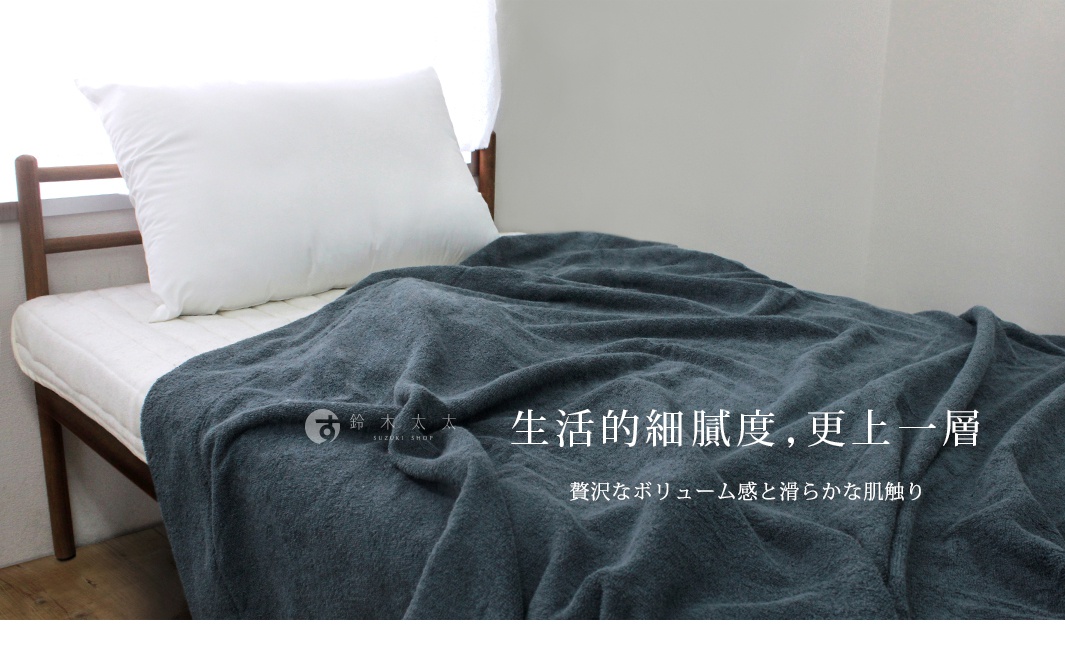 深灰色毛巾被鋪在單人床上，搭配白色枕頭。毛巾被材質柔軟，呈現蓬鬆的織紋。