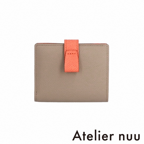 Atelier nuu 灰色皮革雙折短夾，配有珊瑚橙色搭帶，背景為白色。