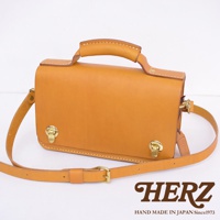 職人手作皮革經典兩用雙扣迷你單肩包，呈現溫潤的駝色，包身結構方正，頂部設有提把，附有可調節的長斜背帶，正面有雙金屬鎖扣設計，材質為天然皮革。