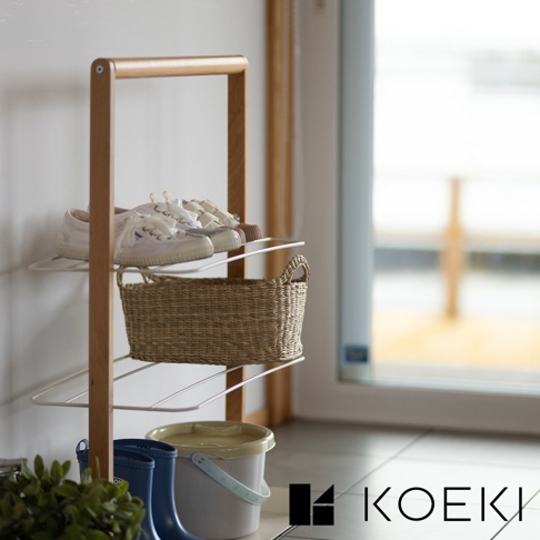 木質邊框搭配白色層架的鞋架，架上擺放著一雙白色帆布鞋和一個編織提籃。下方有藍色雨靴和黃色水桶。