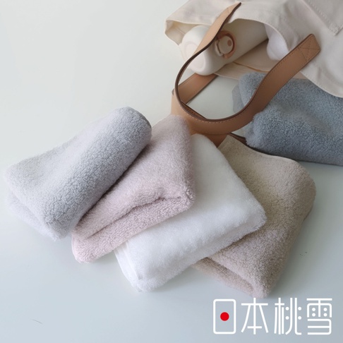 日本桃雪今治棉蕾超無撚蓬鬆毛巾，展示了五種柔和色彩的毛巾，整齊疊放在一起，其中一條淺灰色毛巾擺在最上面。背景是一個帆布袋，裡面裝有白色水瓶和一個淺棕色的皮革提把。