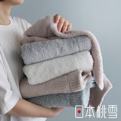 一位女子手捧著一疊顏色柔和的毛巾，上面印有「日本桃雪」的標誌。