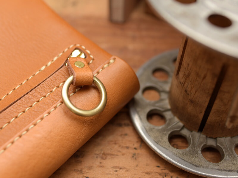 職人手作皮革長夾，採用淺棕色皮革，車線細緻，附有黃銅色金屬拉鍊與 D 型環，質感溫潤。