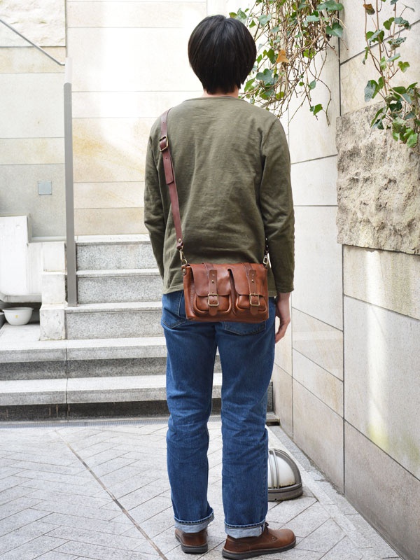 皮革水洗加工前雙口袋肩背包，採用棕色皮革製成，設有雙前袋和翻蓋設計，可斜肩背。