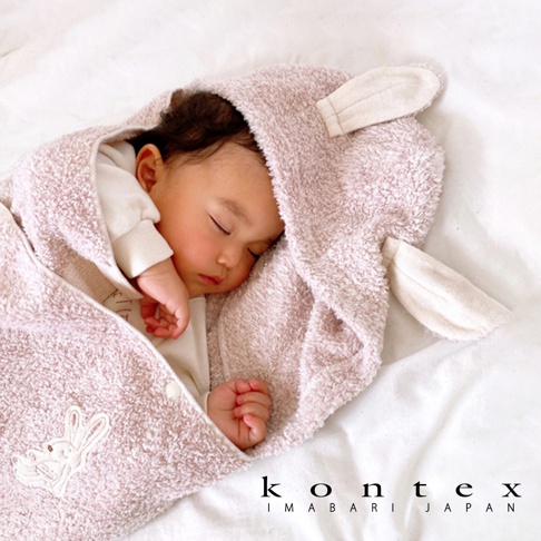 粉紅色厚感兔耳連帽浴巾包裹著熟睡的嬰兒，浴巾上繡有白色兔子圖案，材質柔軟蓬鬆。