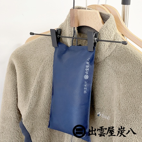 深藍色紋理布料製成的長條形調濕木炭包，懸掛於毛衣外套上，上方有黑色夾子固定。