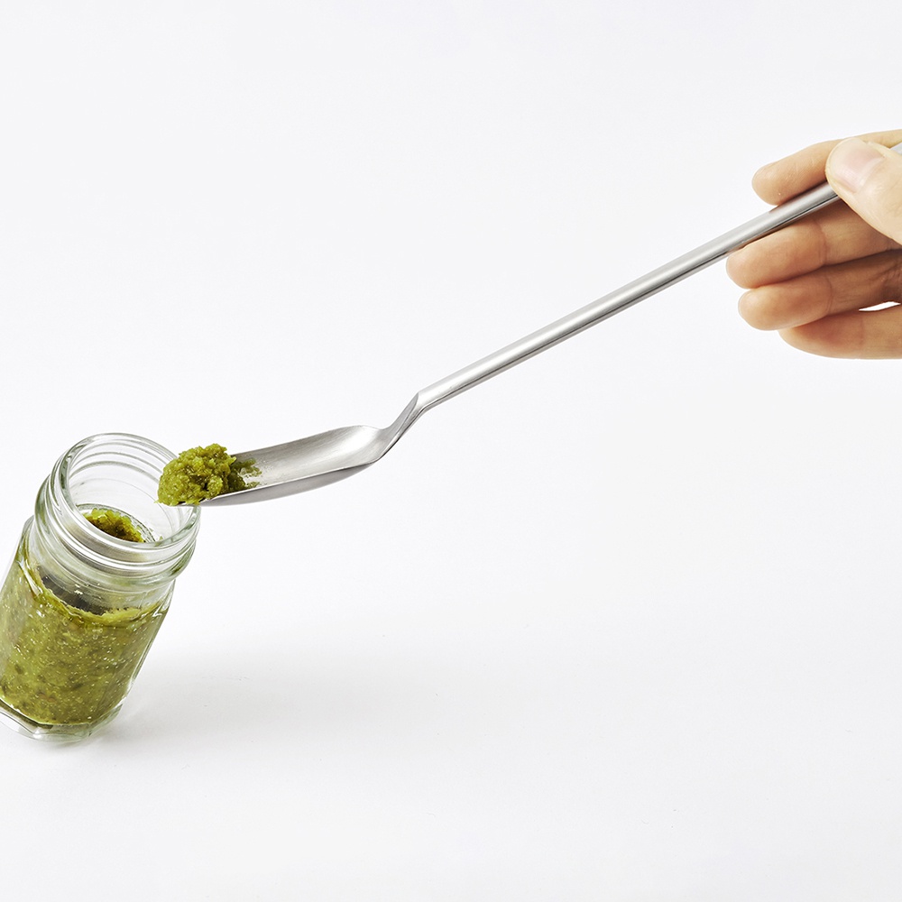 日製小長勺，採用銀色不鏽鋼材質，勺頭呈扁平橢圓形，配有細長手柄，正從一個裝有綠色醬料的玻璃小罐中舀取醬料。