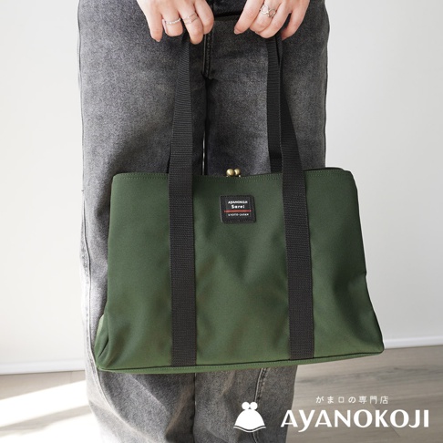 穿著牛仔褲的人手持綠色 AYANOKOJI Sarei 機能布中型口金托特包，包上有名為「AYANOKOJI Sarei KYOTO-JAPAN」的標籤。