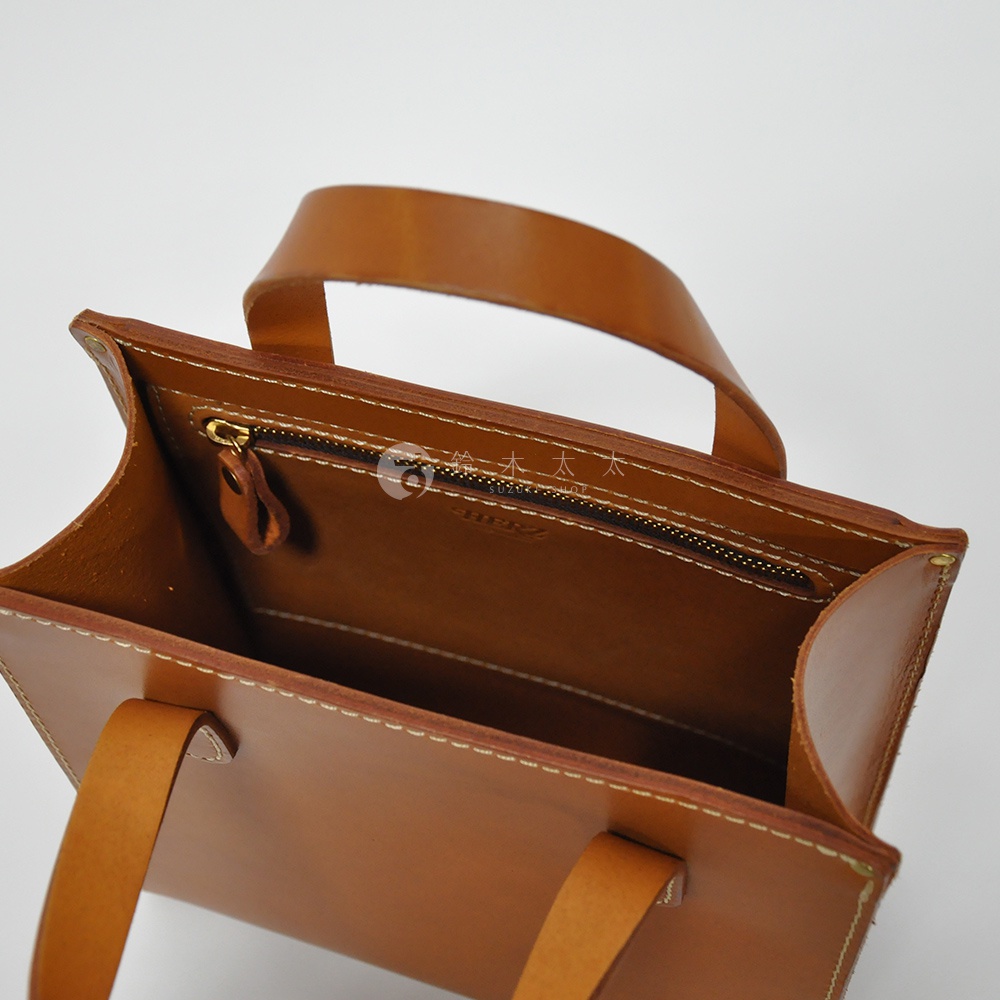 職人手作皮革直式托特包，淺棕色，整體以精緻車縫線勾勒包身，設有金色拉鍊內袋及同色系皮革提把。