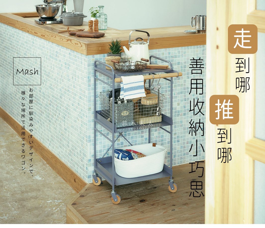 Mash 手推式三層置物收納架，灰色金屬材質，配有木質手柄和四個木輪。置物架上層擺放著金屬網籃、毛巾和茶壺，中層有金屬網籃，下層有一個白色編織收納筐。