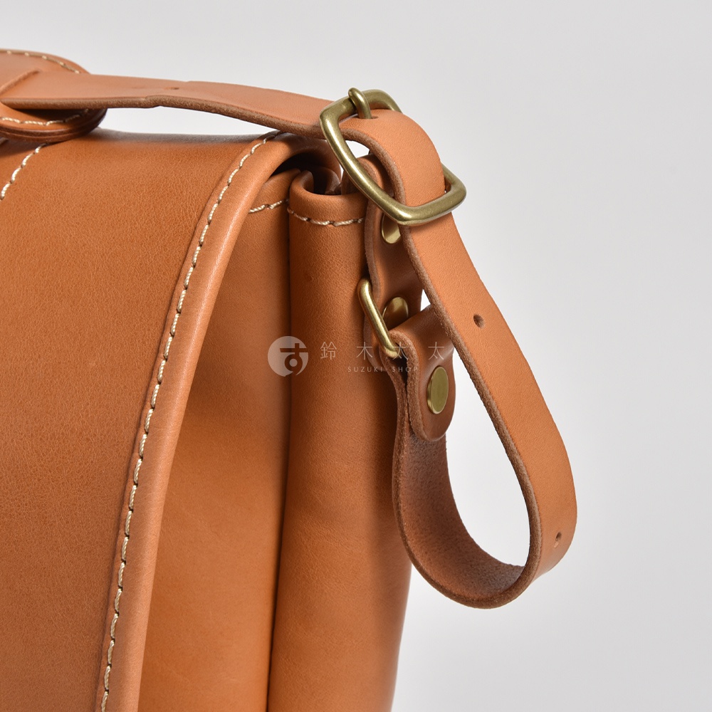 職人手作皮革復古郵差包 CM-100，採用淺棕色皮革製作，搭配金色金屬扣環和鉚釘。包包側面有精緻的縫線裝飾，整體呈現復古風格。