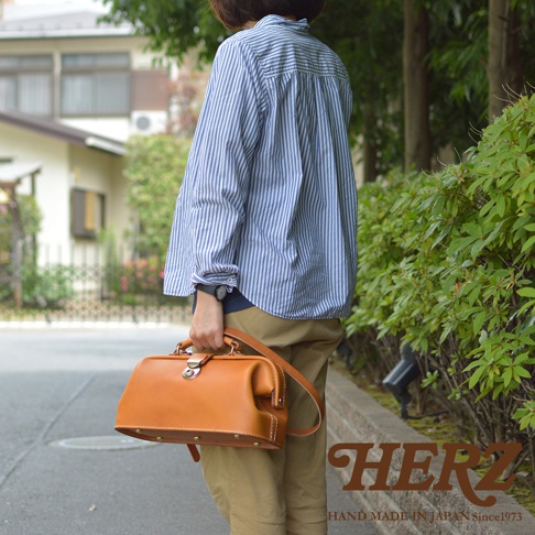 職人手作皮革長型迷你醫生包，採用光滑的棕褐色皮革製成，配有銀色金屬扣環和提把，側面有鉚釘裝飾。