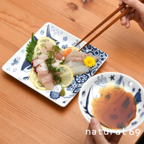 印有藍色海洋生物圖案的白色方形陶瓷餐盤，盛有生魚片、檸檬片和芥末。