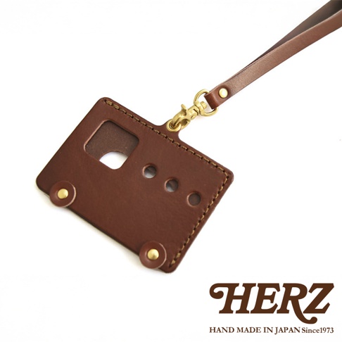 日本HERZ職人手作皮革交通卡收納夾，這款深棕色皮製卡套以其獨特的老式交通卡造型設計，配有可調節的掛繩和黃銅扣環，並印有HERZ品牌標誌及「HAND MADE IN JAPAN Since1973」字樣，彰顯其精湛的日本手工藝。