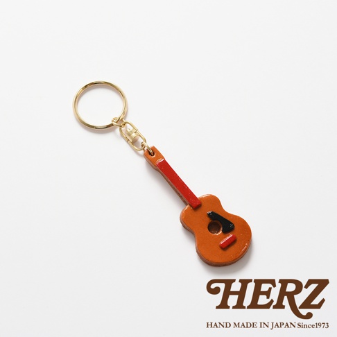 職人手作皮革吉他造型鑰匙圈，以棕色皮革製作吉他主體，搭配紅色皮革琴頸與琴橋，黑色皮革裝飾，並附有金色金屬鑰匙圈。