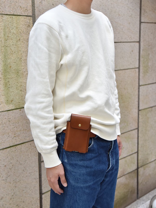 棕色皮革製成的手機收納包，附有金屬釦，可掛於腰帶上。