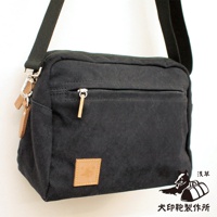 黑色石洗帆布旅行側背包，帶有拉鍊前袋、皮革標籤和可調式肩帶。