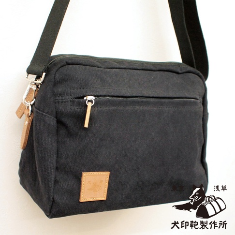 黑色石洗帆布旅行側背包，帶有拉鍊前袋、皮革標籤和可調式肩帶。