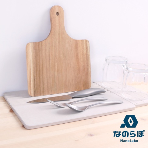 淺灰色珪藻土吸水墊上，擺放著一把銀色金屬刀、一把銀色金屬叉和一把銀色金屬湯匙。後方有兩個透明玻璃杯，一個木質砧板立在後方。