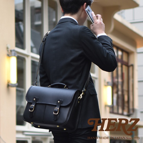 黑色皮革製成的手提/單肩兩用包，帶有兩個金屬扣環和可調節肩帶，適合商務或休閒場合。