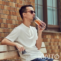 男子手持TO GO BOTTLE雙層隨手瓶，瓶身透明，內有茶色飲品，瓶蓋為深灰色，搭配白色短袖上衣和藍色短褲，坐在木質長凳上。