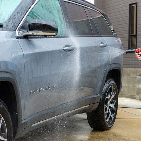 灰色吉普車正在被沖洗，水流噴灑在車門上，車身側面可見「COMMANDER」字樣。