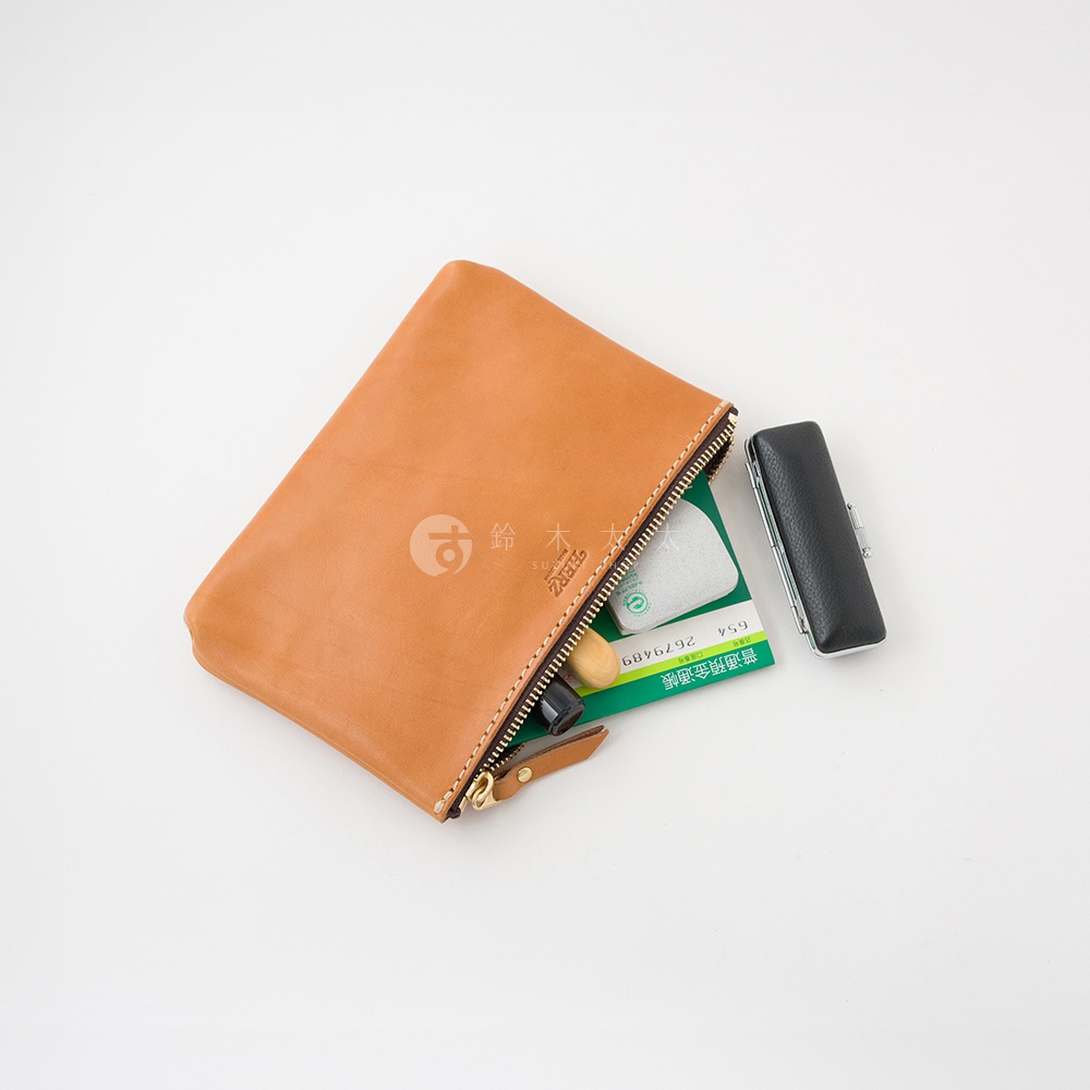 職人手作皮革長方形拉鍊收納包，淺棕色皮革，拉鍊開合，內含綠色卡片、印章及口紅。