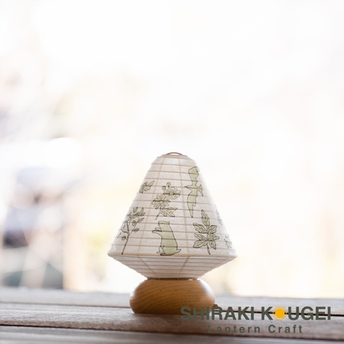 八女迷你裝飾提燈，燈罩為錐形，淺米色紙質，印有綠色植物與小動物圖案，底部為圓形木質底座。