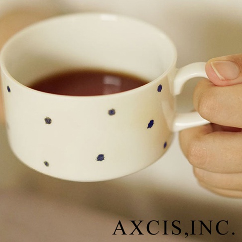 手繪美濃燒馬克杯，白色杯身點綴不規則藍色圓點，附有白色手柄，盛有深色飲品。