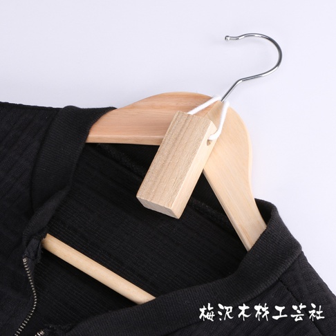 木質衣架上掛著一件黑色衣物，衣架上有一個綁著白色細繩的天然未上漆樟木條，木條呈長方形，兩端有孔。