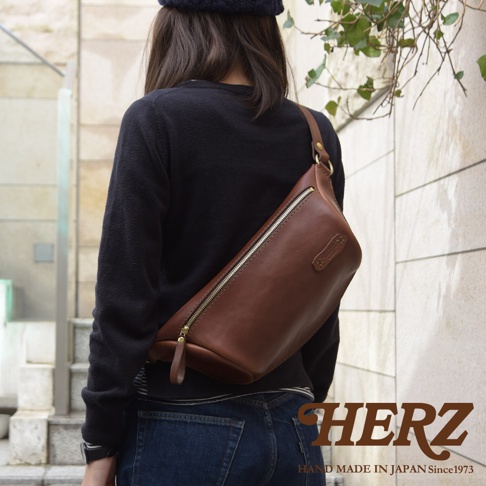 職人手作皮革輕便斜背包，棕色皮革材質，配備金色拉鍊與五金配件，斜背於身，簡約實用。