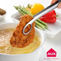 leye 靈活炸物夾，不鏽鋼材質，以夾子夾住一塊金黃酥脆的炸物，炸物正從冒泡的熱油中取出，背景有蘆筍、紅黃甜椒。