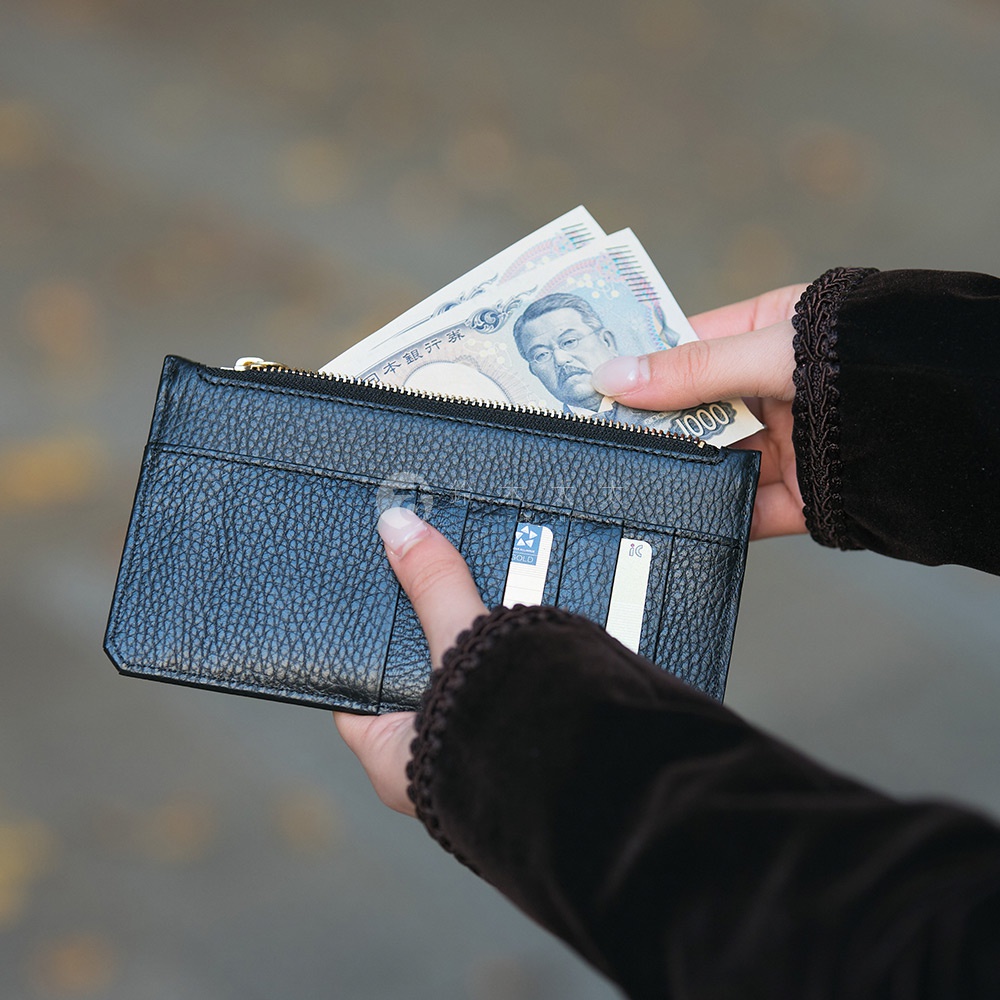 一張手持黑色皮革長夾的特寫照片，夾中露出日圓鈔票，鈔票上可見人物肖像和數字1000。