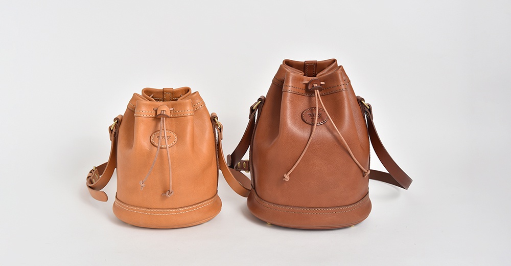 兩款皮革束口單肩包，分別為淺棕色與深棕色，皆有品牌壓紋及束繩設計。