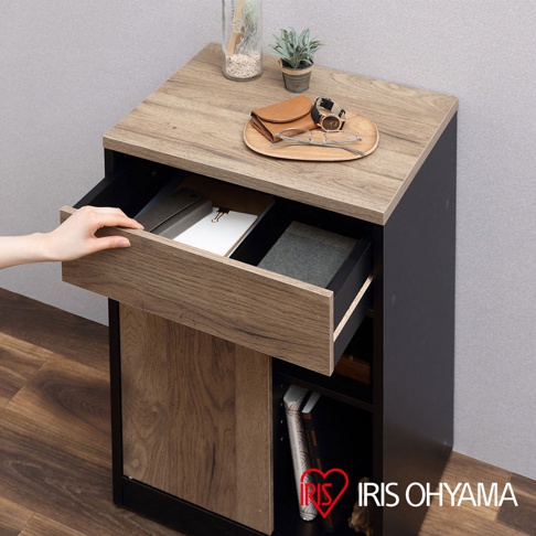 木質抽屜收納櫃，頂部為仿木紋桌面，側面為黑色，配有兩個木紋飾面抽屜，其中一個抽屜部分拉開，內有文件。櫃子下方為開放式層架，展示書籍。