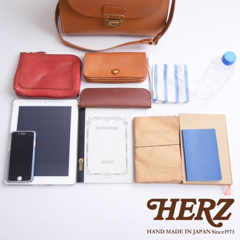 HERZ 品牌皮革包，內容物包含手機、平板、筆記本、水壺、毛巾及兩個皮革小物包，整體為俯視拍攝。