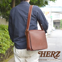 一個人肩背著日本HERZ手工製作的棕色皮革斜背包，背包上有一個Z字壓印。